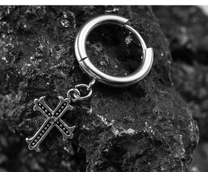 Macro detail of gothic cross earring with embossed dots on a grey stone texture