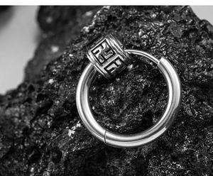 Macro shot of vintage titanium steel hoop earring with engraved cylinder pendant on lava rock