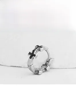 Close-up of silver punk hoop earrings with black cross motifs on stone surface