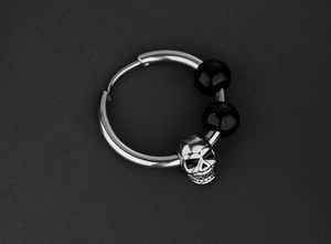 Détail d'une boucle d'oreille tête de mort argentée punk avec des perles noires