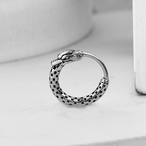 Minimalist silver dragon head earring with checkered pattern band on stone background