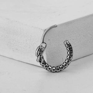 Minimalist dragon head steel earring with checkered texture on white stone background
