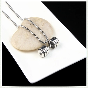 Macro shot of silver stainless steel dumbbell pendant on pebbles for fitness jewelry