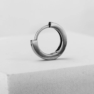 Minimalist silver stainless steel hoop earrings with a brushed metal texture on a stone pedestal