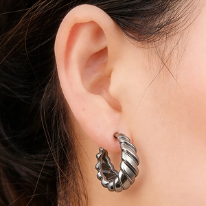 Close-up of a silver ribbed huggie earring with twisted texture worn by a male model