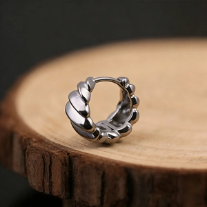 Macro shot of silver-tone striped textured hoop earring on a wooden base