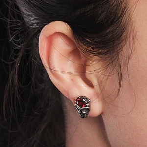 Gothic skull stud earrings in vintage silver with a red zircon stone worn on the ear