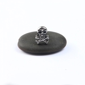 Clou d'oreille punk tête de mort et os croisés en acier argenté vintage sur un galet