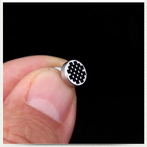 Vue macro d'une boucle d'oreille haltère en acier titane argenté à motif damier noir