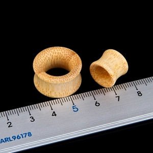 Natural hollow bamboo double flare ear gauges with textured wood grain on black background