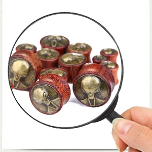 Detailed view of wooden ear plugs with bronze alien head relief in various sizes