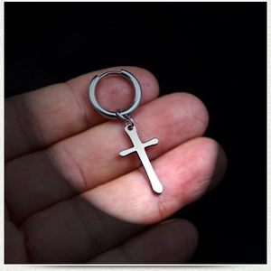 Gros plan de la boucle d'oreille croix en acier inoxydable poli sur fond sombre