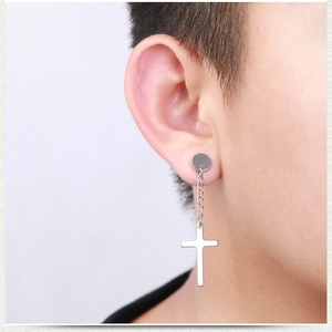 Close-up of a silver stainless steel cross earring with chain on a person's ear