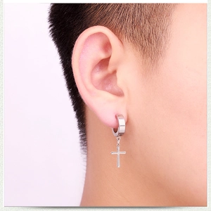 Close-up of a silver polished stainless steel cross pendant earring on a model ear