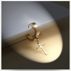 Macro shot of gold cross charm earring with polished stainless steel finish on silk