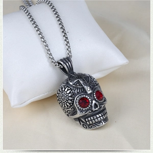 Gothic skull pendant necklace with red gem eyes and floral engravings on white pillow