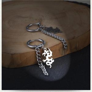 Detalle de pendientes de aro con dragón plateado y cadenas sobre fondo de piedra rústica