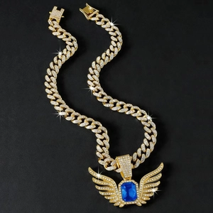 Macro detail of iced-out hip hop wing pendant with blue gem and golden cuban chain