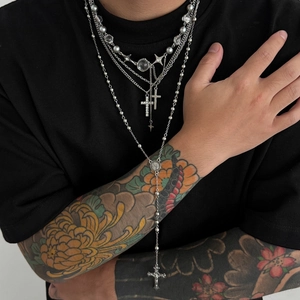 Détail de colliers argentés superposés avec pendentifs croix et perles sur t-shirt noir