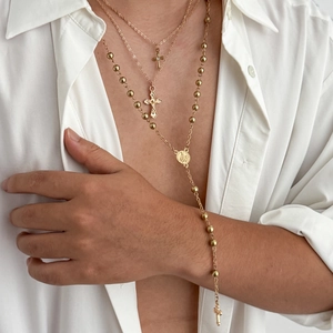 Détail de colliers dorés superposés avec pendentif croix et médaillon sur chemise blanche