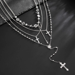Détail de colliers multicouches argentés avec pendentifs croix et perles sur roche sombre