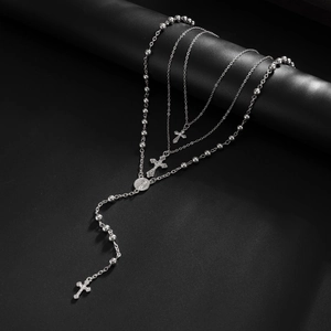 Gros plan de colliers superposés argentés avec pendentifs crucifix et médaille religieuse