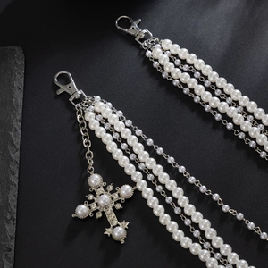 Détail d'une chaîne de pantalon multicouche en perles blanches avec pendentif croix