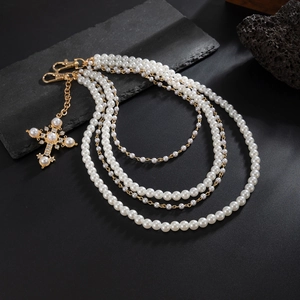 Macro detail of multi-layer pearl necklace with ornate gold cross pendant on dark stone