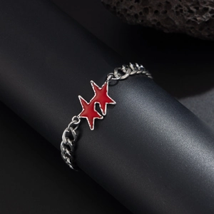 Dettaglio macro del bracciale a catena NK argento con ciondoli a stella rossi su roccia