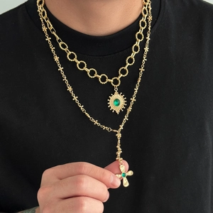 Gold layered necklace with green gem sunflower and cross pendants on black shirt