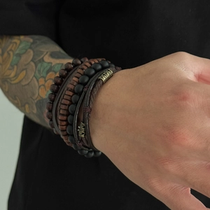 Macro detail of men's multilayered leather and wooden bead bracelets with vintage metal clasp