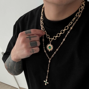 Detailed view of layered gold cuban chain and cross necklace with green gemstones