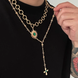 Detail of layered gold necklaces with cross pendant and green gemstone on black tee