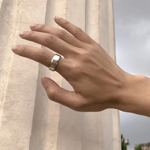 Bague en métal argenté poli avec motif géométrique portée au doigt en extérieur naturel