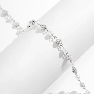Detailed close-up of pearl necklace with silver pavé diamond beads on white stand