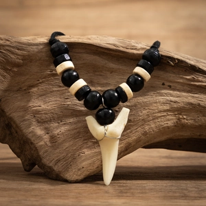 Détail d'un collier en perles de bois avec pendentif dent de requin sur bois rustique