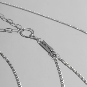 Close-up of industrial multi-layer silver body chain with ENCHANTED engraved metal tag