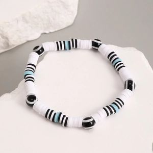 Macro detail of handmade heishi bead bracelet on stone, featuring striped accent beads