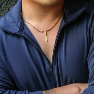 Close-up of minimalist gold bar pendant necklace on male model with box chain