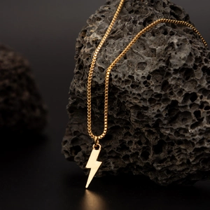 Polished gold lightning bolt pendant on a box chain draped over black volcanic rock