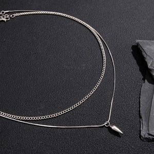 Detail of double layered silver punk necklace with minimalist cone pendant on dark rock