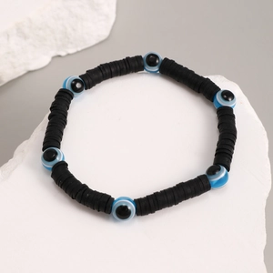 Close-up of black heishi beads and blue evil eye charms on an elastic bracelet