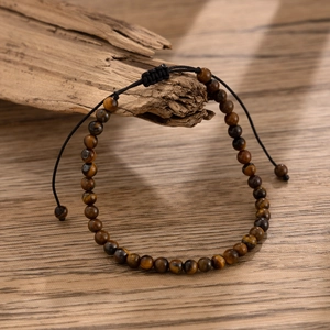 Macro detail of men's tiger eye stone anklet with adjustable black braided cord on wood