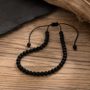 Detail of adjustable black matte stone beads on a rustic wooden surface with braided cord