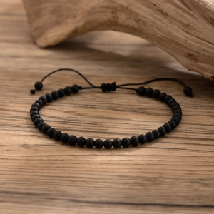 Detail of matte black beaded anklet with adjustable sliding knot on wooden background