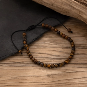 Men's tiger eye beaded anklet with adjustable black braided cord on a rustic stone background