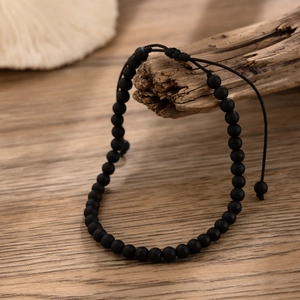 Adjustable matte black tiger stone beaded anklet displayed on natural driftwood