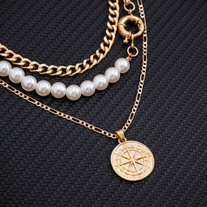 Vue détaillée d'un collier doré multi-rangs avec perles et pendentif boussole