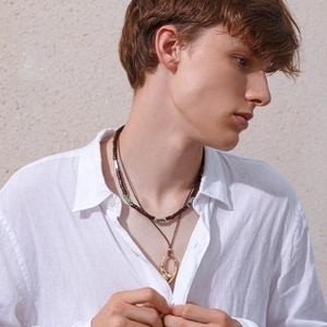 Detail of men's layered wooden bead necklace and golden oval pendant on linen shirt