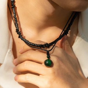 Dettaglio di collane a strati da uomo con perle di legno nere e ciondolo in malachite